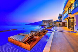 A modern resort with an infinity pool, wooden loungers, and a view of the ocean. - Villa Overseas Views (Unknown)