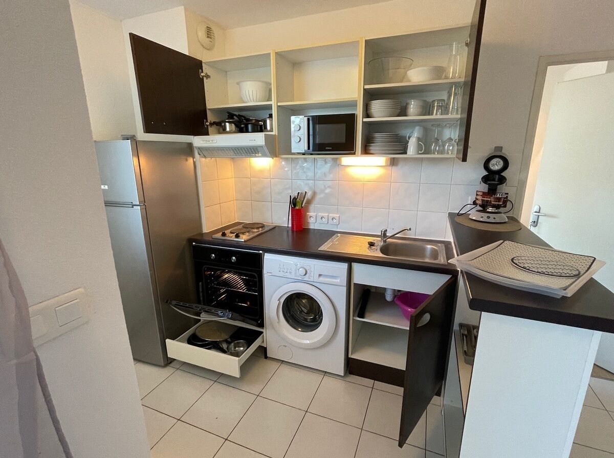 Une cuisine compacte équipée d’un lave-linge intégré, d’un four à micro-ondes et d’un évier.
