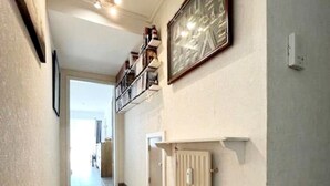 Un pasillo con un radiador, un cuadro enmarcado y una estantería con libros.