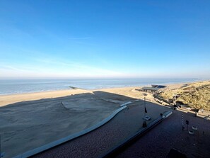 Ein Strand mit freiem Blick auf den Ozean, einem Sandbereich und einem Gebäude mit flachem Dach.