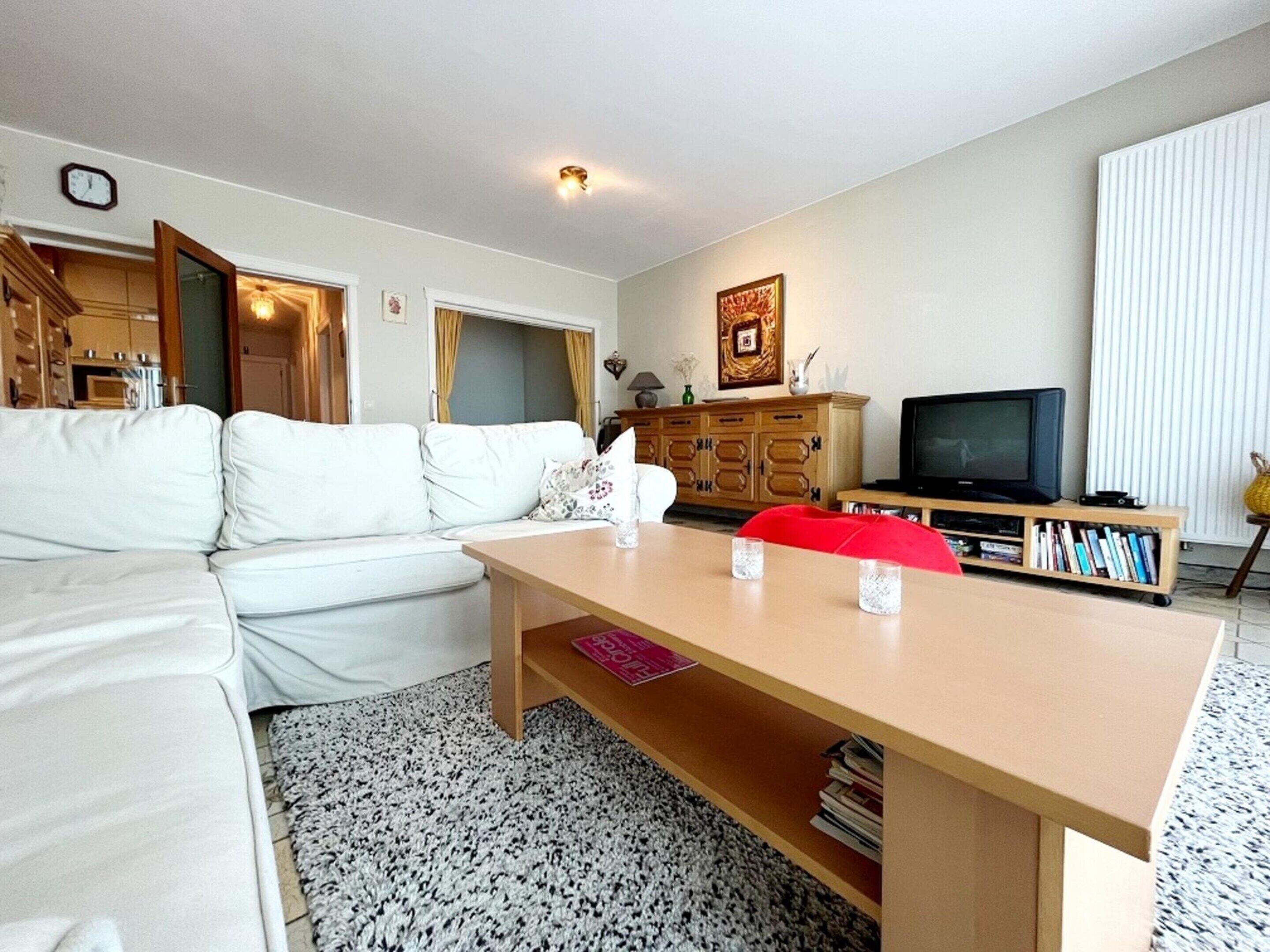 A living room with a white sofa, a wooden coffee table, a television, and a bookshelf.