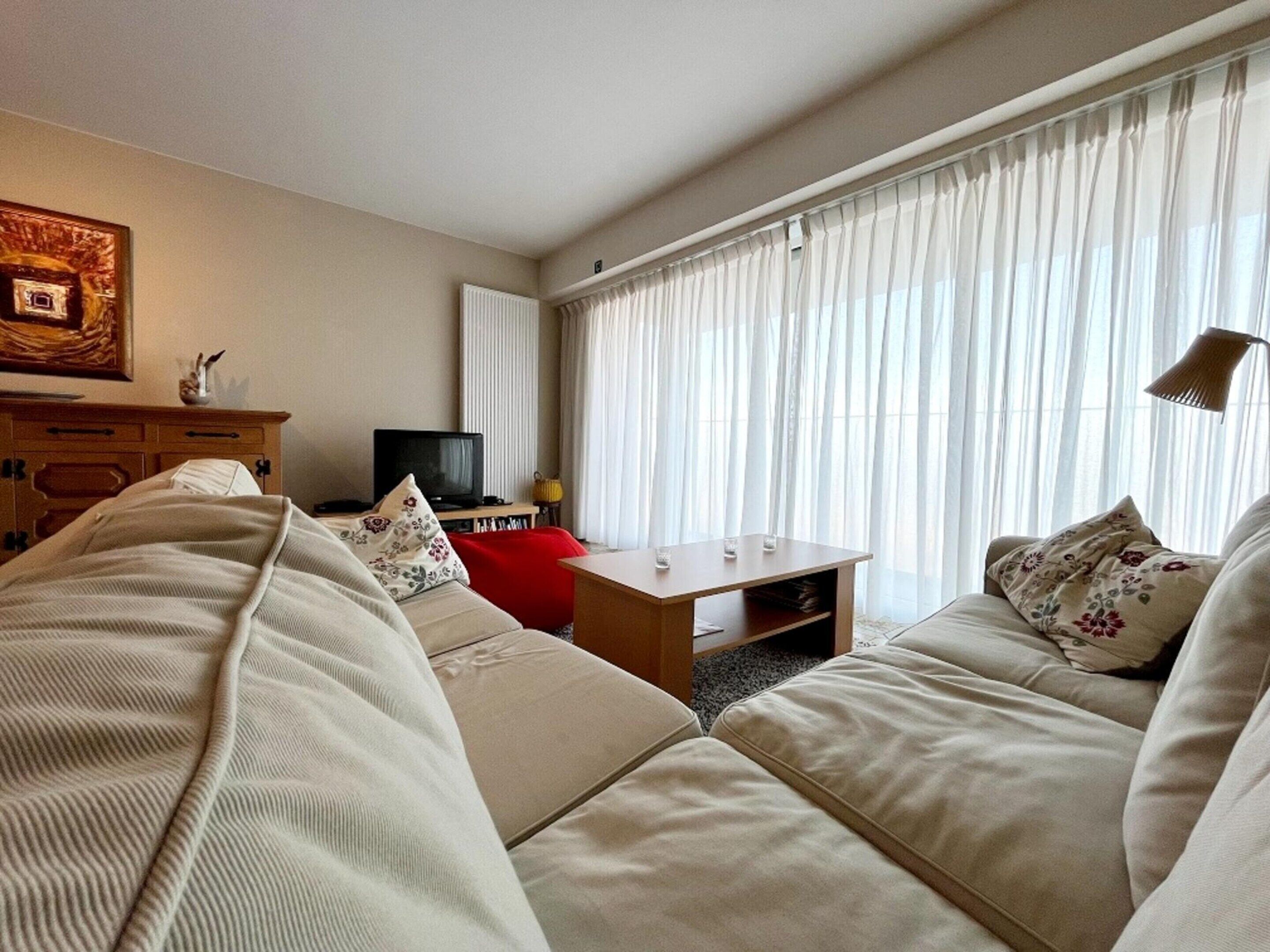 Una sala de estar moderna con un sofá beige, un sillón rojo, una mesa de centro de madera y un televisor.