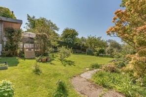 A well-maintained garden with a paved path, a wooden deck, and various potted plants.