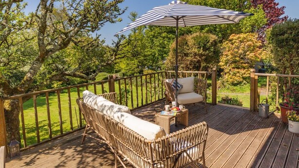 Une terrasse en bois avec des meubles en osier, un parasol à rayures et une vue sur le jardin.
