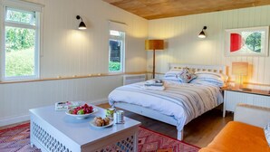 Une chambre à coucher comprenant un lit, des tables de chevet, une commode, une fenêtre et une vue sur la verdure à l’extérieur.