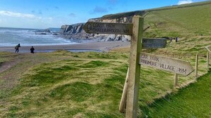 Un panneau indicateur en bois indiquant la direction du « sentier côtier de Challabrough » et du « parking du village de Ringmore ».