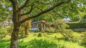 Une maison entourée d’une végétation luxuriante et bordée d’un petit étang.