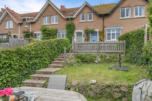 Un quartier résidentiel avec un escalier en bois menant à une maison dotée d’une porte bleue, entourée de verdure et d’un petit jardin.
