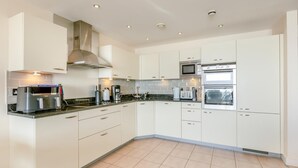A modern kitchen with white cabinets, a stainless steel range hood, a microwave, an oven, and a coffee maker. - 3 Bed in Torquay (oc-a31052) (Torquay)