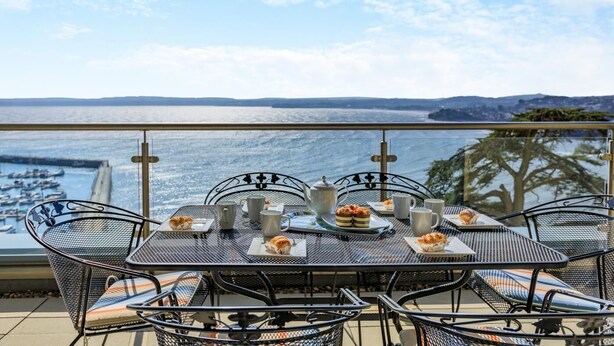 A table set with plates, cups, and a teapot, overlooking a body of water with boats and a distant shoreline. - 3 Bed in Torquay (oc-a31052) (Torquay)