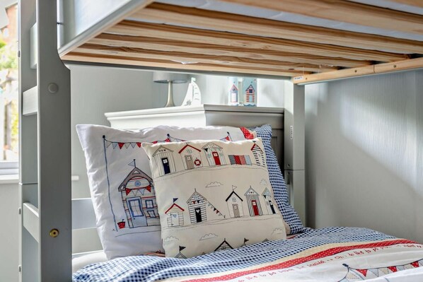 Una cama litera con cubrecama a cuadros y almohadones decorativos con motivos marinos.