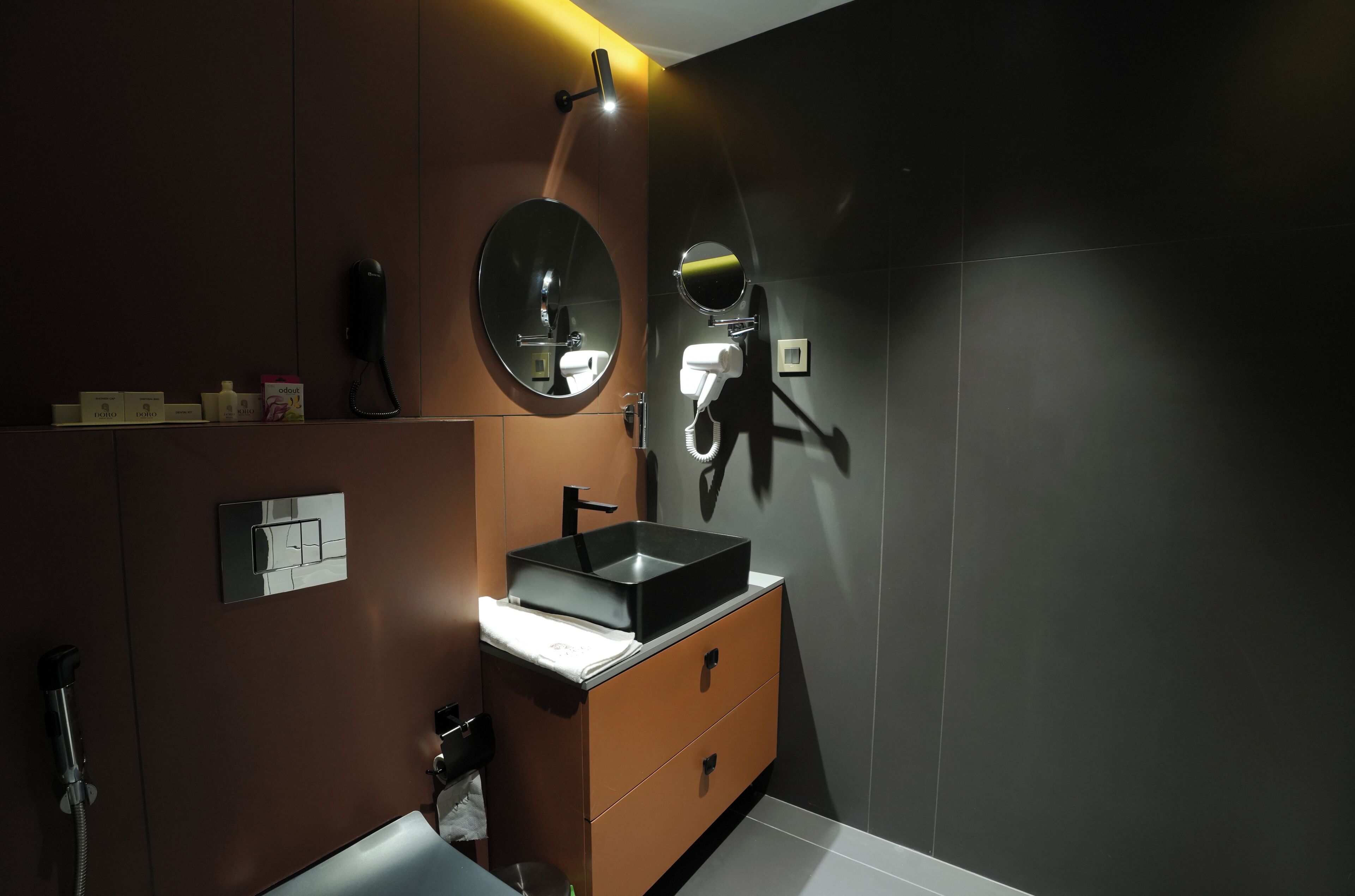 Un bagno moderno con una parete scura, uno specchio rotondo, un lavandino nero e un soffione a mano.