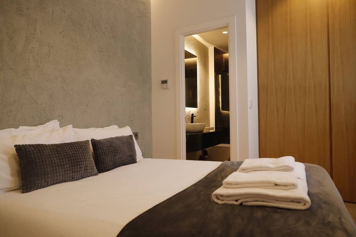A hotel room with a bed, a wooden wardrobe, and a bathroom visible through an open door.