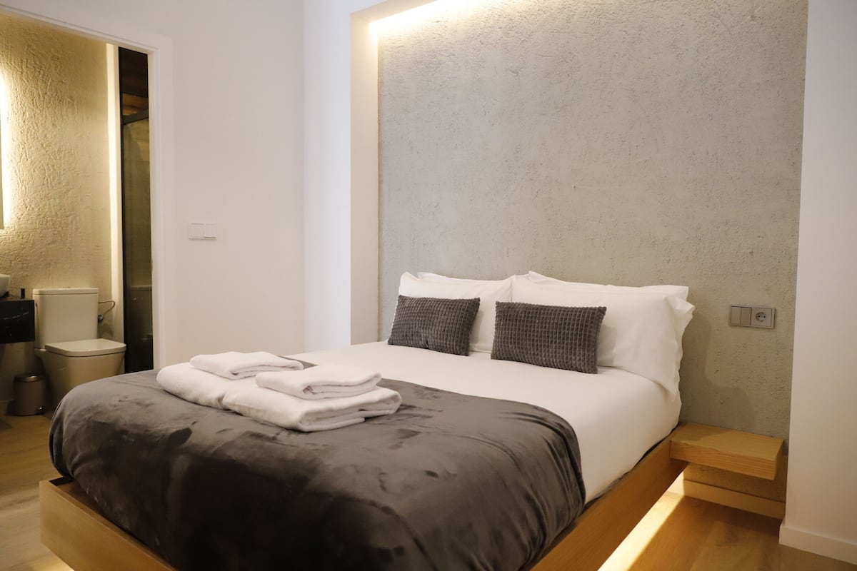 A modern bedroom with a bed, bedside tables, and a bathroom visible in the background.