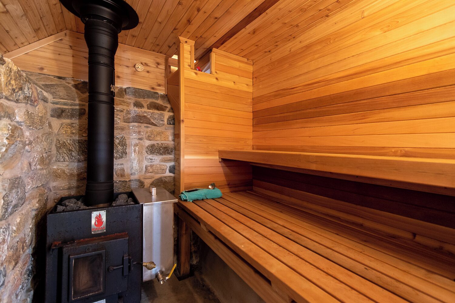 Eine Sauna mit Steinwand, schwarzem Ofen und Holzbänken.