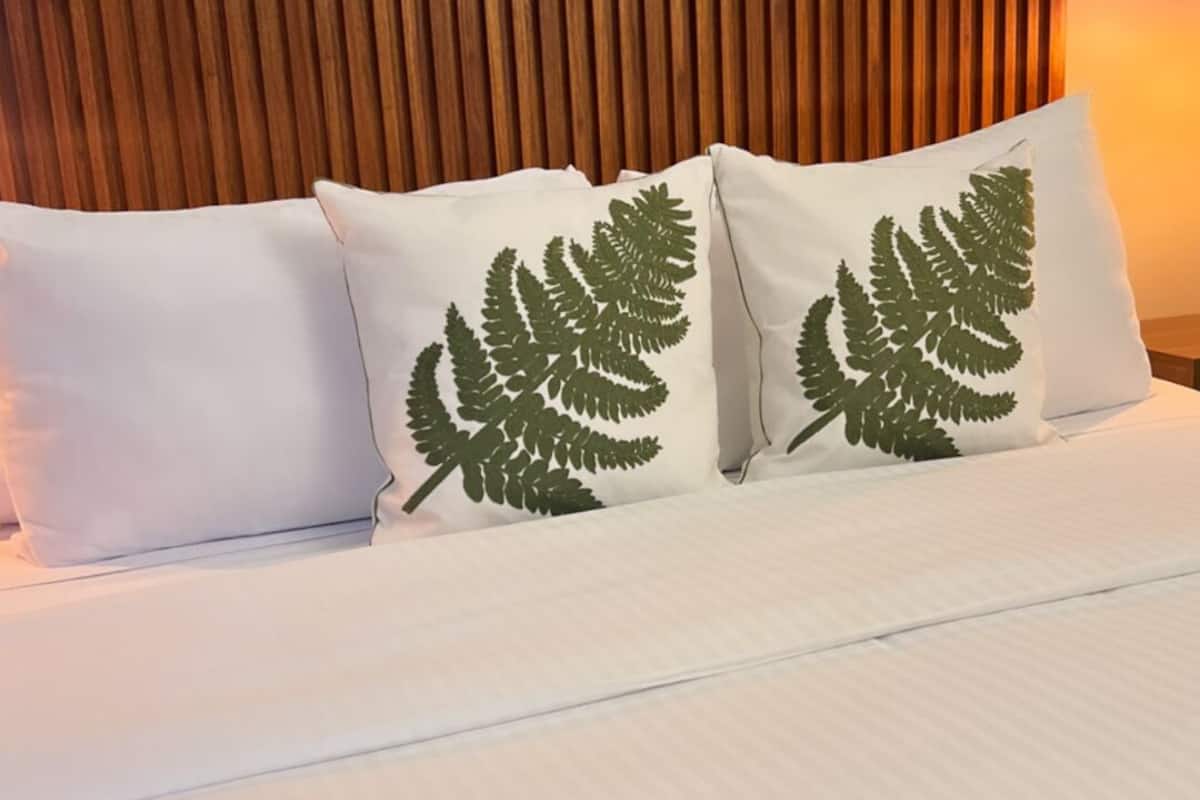 Una cama con ropa blanca y dos almohadas con diseño de hojas de helecho.