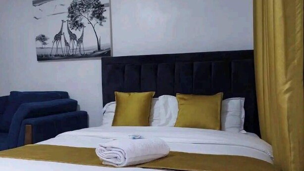A neatly made bed with white and gold bedding, a dark headboard, and a single artwork on the wall.