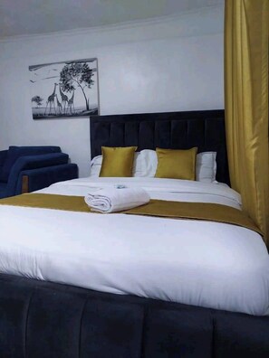 A neatly made bed with white and gold bedding, a dark headboard, and a single artwork on the wall.