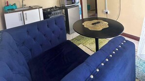 A compact living space with a blue sofa, a small kitchen area including a stove and microwave, and a flat-screen TV mounted on the wall.