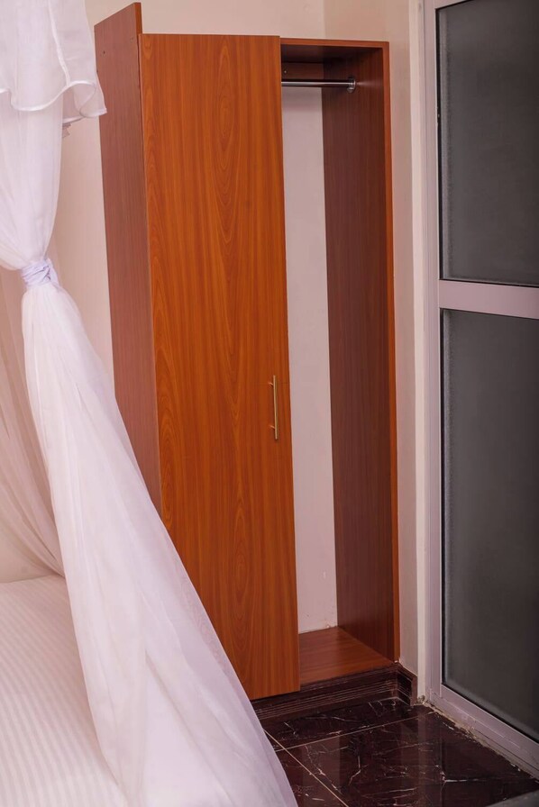 A wooden wardrobe with a sliding door, a bed with a white canopy, and a dark tiled floor.