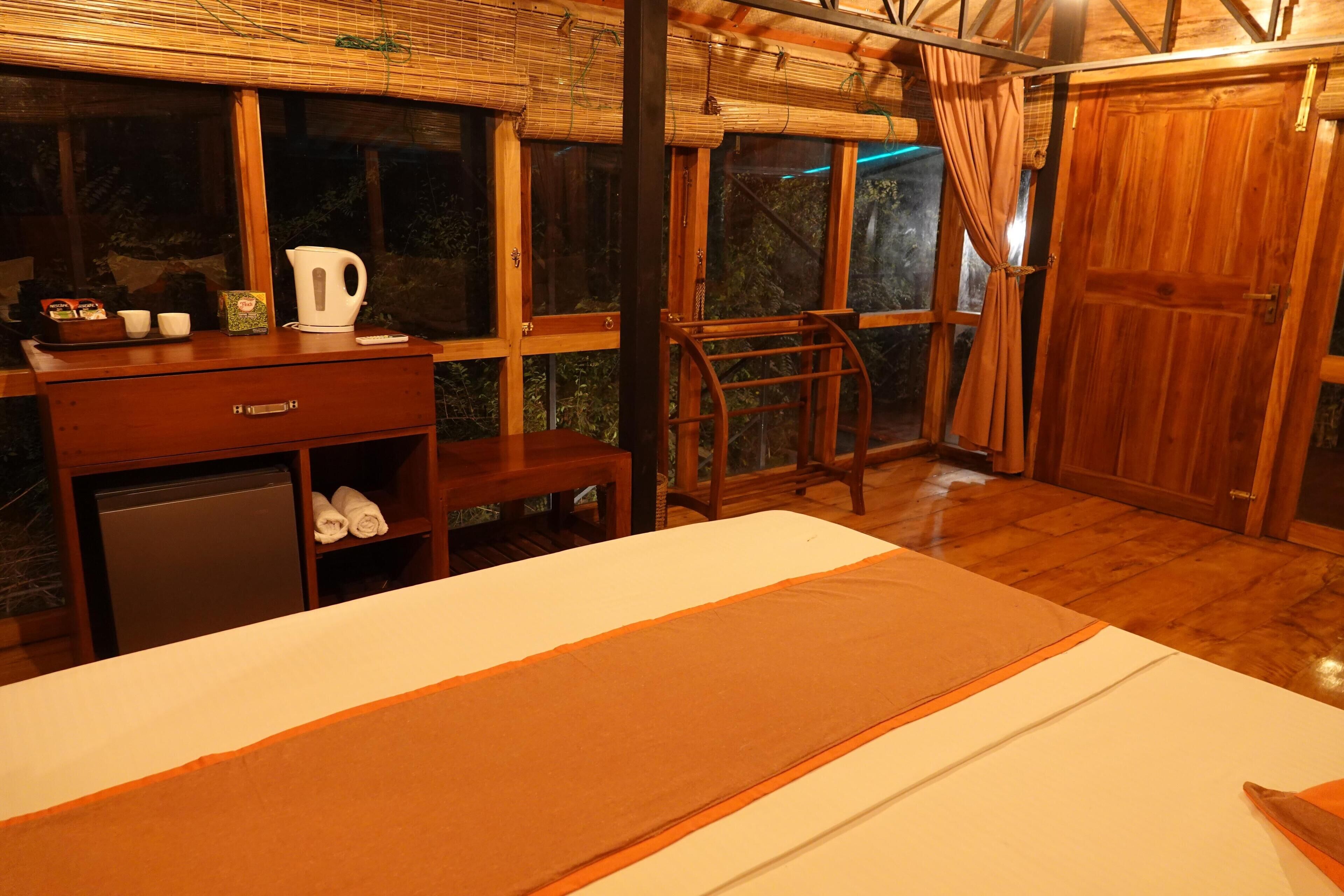 A room with a bed, a desk with a kettle, and a small refrigerator.