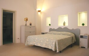 Cozy retreat with a neatly made bed, bedside table, and nightstand, featuring a door to a separate area and wall-mounted mirrors.