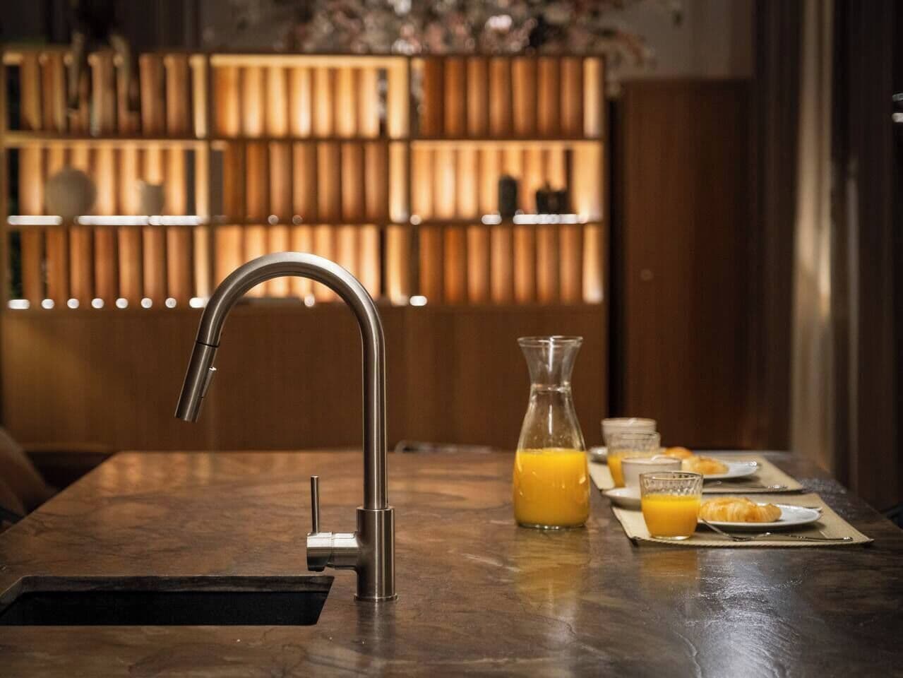 Eine moderne Küche mit einem Edelstahlarmaturen, einem Glas mit Orangensaft und Frühstücksgebäck auf einer Marmarbeplatte.