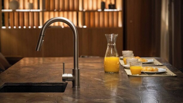 Een moderne keuken met een roestvrijstalen kraan, een glazen kan sinaasappelsap en ontbijtartikelen op een marmeren aanrecht.