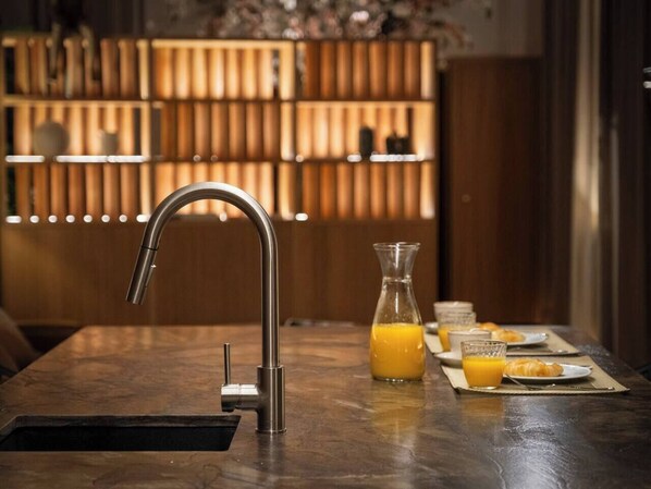 Una cocina moderna con un grifo de acero inoxidable, una jarra de vidrio con jugo de naranja y alimentos para el desayuno sobre una encimera de mármol.