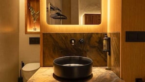 Een moderne badkamer met een grote spiegel, een rond wastafeltje en houten kastjes.