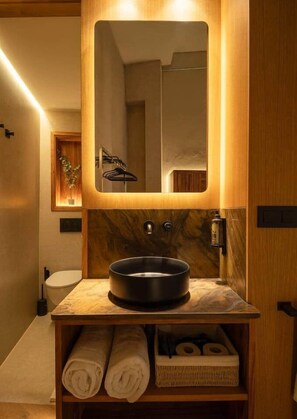 Un baño moderno con un espejo grande, un lavamanos redondo y muebles de madera.