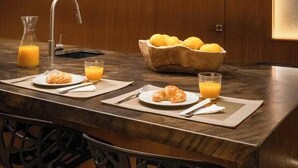 Una cocina moderna con encimera de madera, un lavamanos y un bol con limones. Hay dos platos con cruasanes y vasos de zumo de naranja.