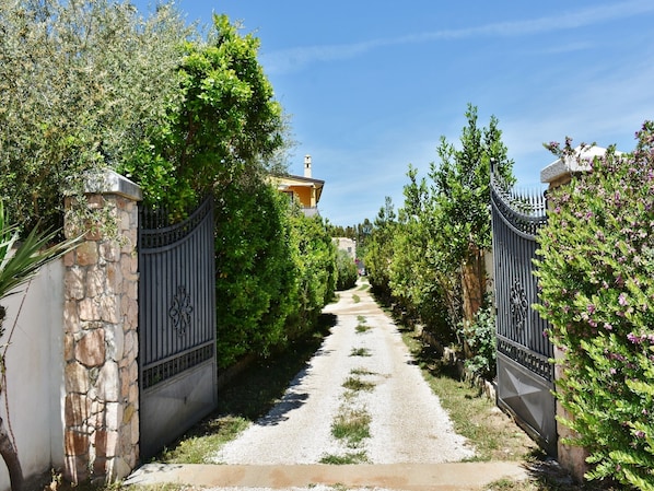 A gravel pathway leading to a gated entrance with stone walls and metal gates.