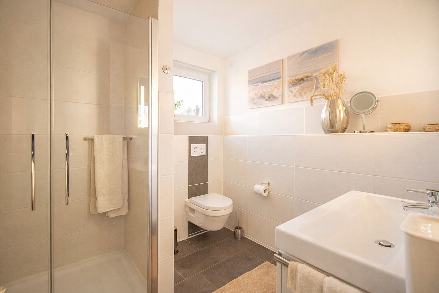 Un baño con cabina de ducha de vidrio, inodoro, lavabo y ventana.