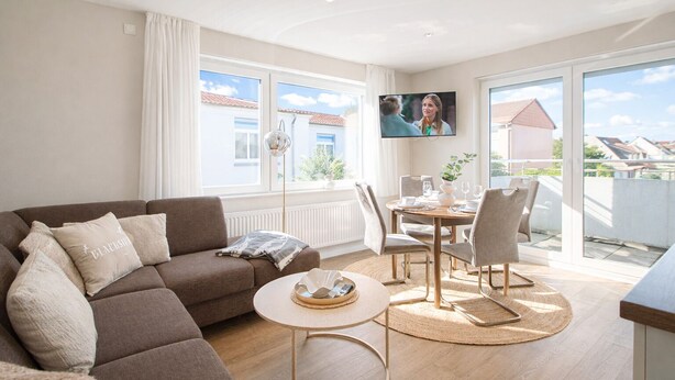 Ein modernes Wohnzimmer mit einer Couch, einem runden Couchtisch und einem Essbereich mit Stühlen und einem Tisch.