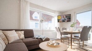 Ein modernes Wohnzimmer mit einer Couch, einem runden Couchtisch, einem Esstisch mit Stühlen und einem an der Wand montierten Fernseher.