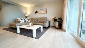 A modern living room with a sofa, coffee table, and a large window. - Apartment in Wenduine With Stunning Sea Views (De Haan)