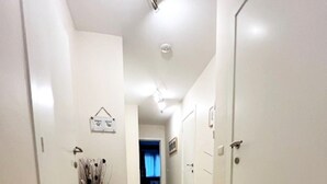 A hallway with white walls and doors, a tiled floor, and a vase with branches on the left. - Apartment in Wenduine With Stunning Sea Views (De Haan)