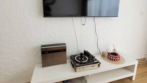Un salon moderne avec un téléviseur à écran plat fixé au mur, une platine vinyle et un meuble de rangement blanc agrémenté d’un tapis tissé et d’objets décoratifs.