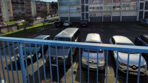 Un parking avec plusieurs voitures, un immeuble à étages doté de balcons et un ciel dégagé.