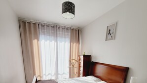 Une chambre à coucher avec un lit en bois, un bureau, une chaise, une commode et un luminaire suspendu.