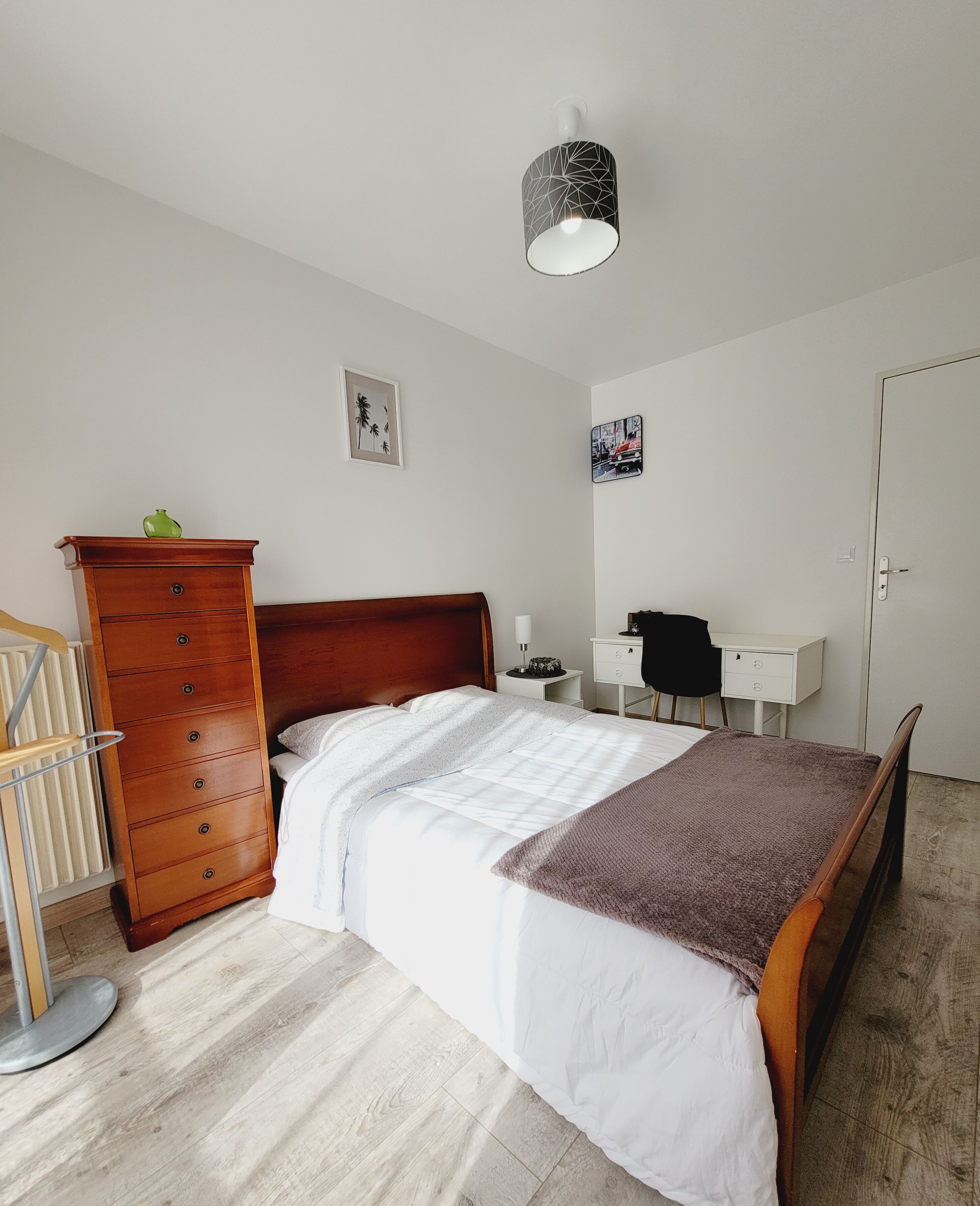 A bedroom with a wooden bed, a dresser, a desk, and a hanging light fixture.