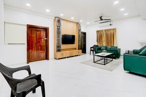Ein modernes Wohnzimmer mit Flachbildfernseher, grünen Sofas, einem Couchtisch und einer Holztruhe.