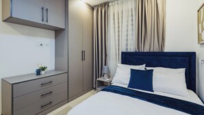 A bedroom with a bed, a nightstand, a dresser, and a wardrobe. - OASIS 2: Stylish 2BR with premium finishes, custom décor & stunning views. (Takoradi)