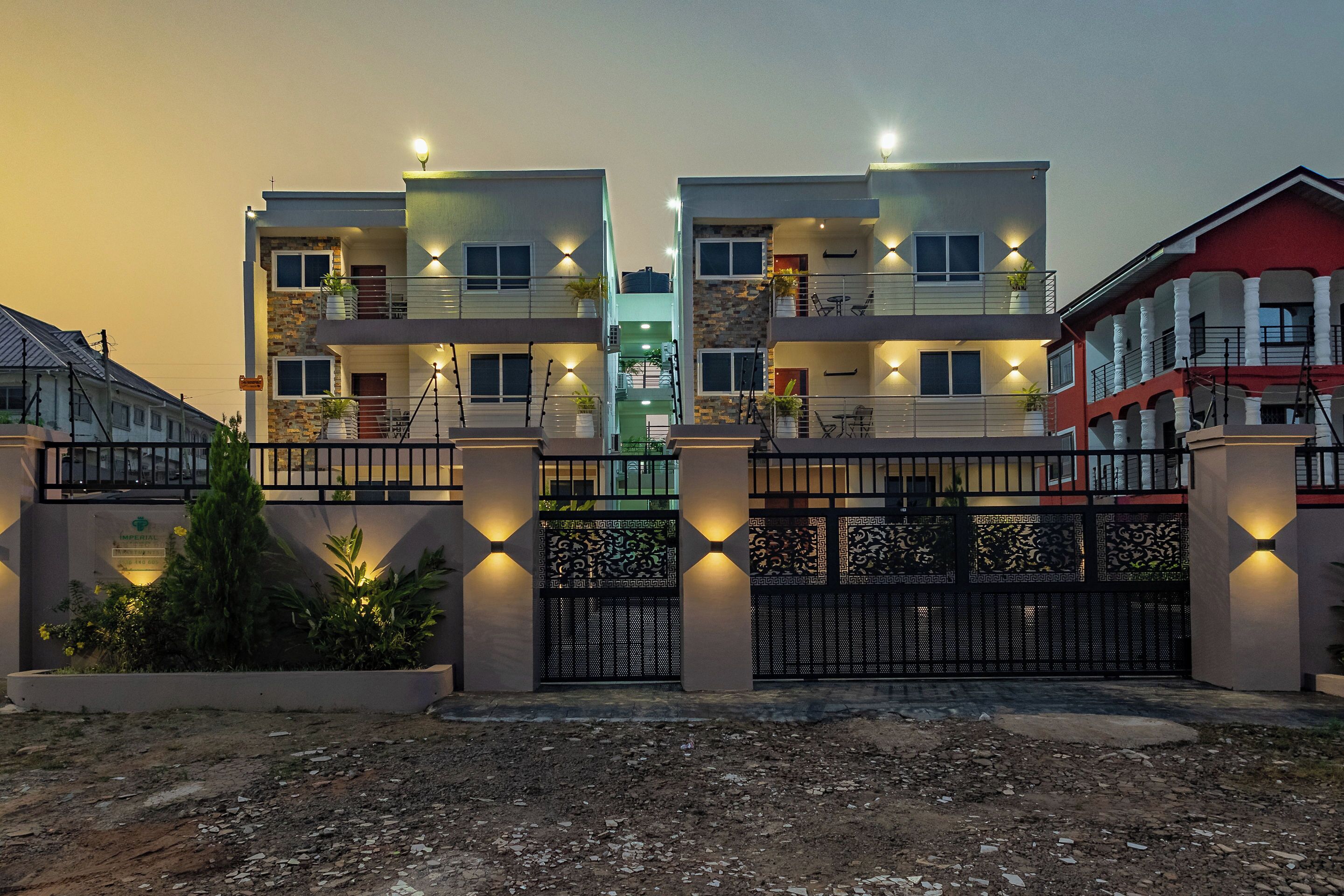 Un immeuble résidentiel moderne à plusieurs étages, doté de balcons, d’une entrée sécurisée et d’un éclairage extérieur.