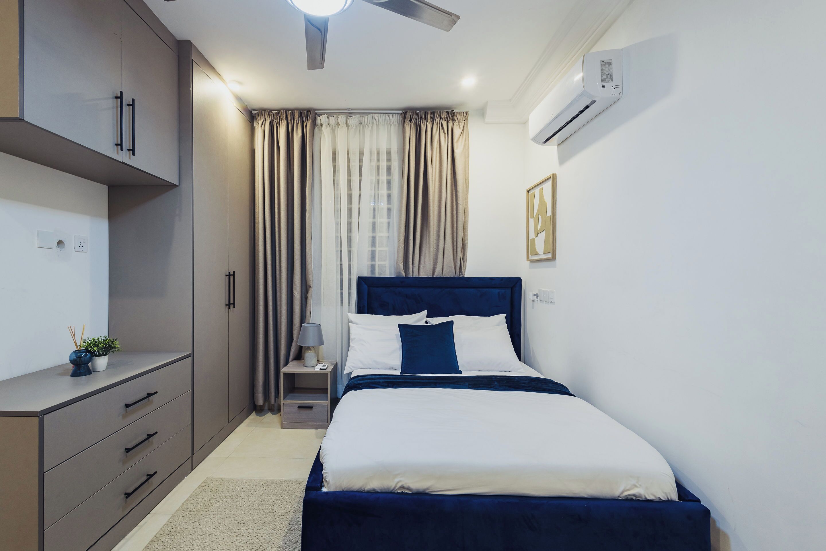 Une chambre moderne comprenant un lit, une table de chevet, une commode, une armoire et un appareil de climatisation.