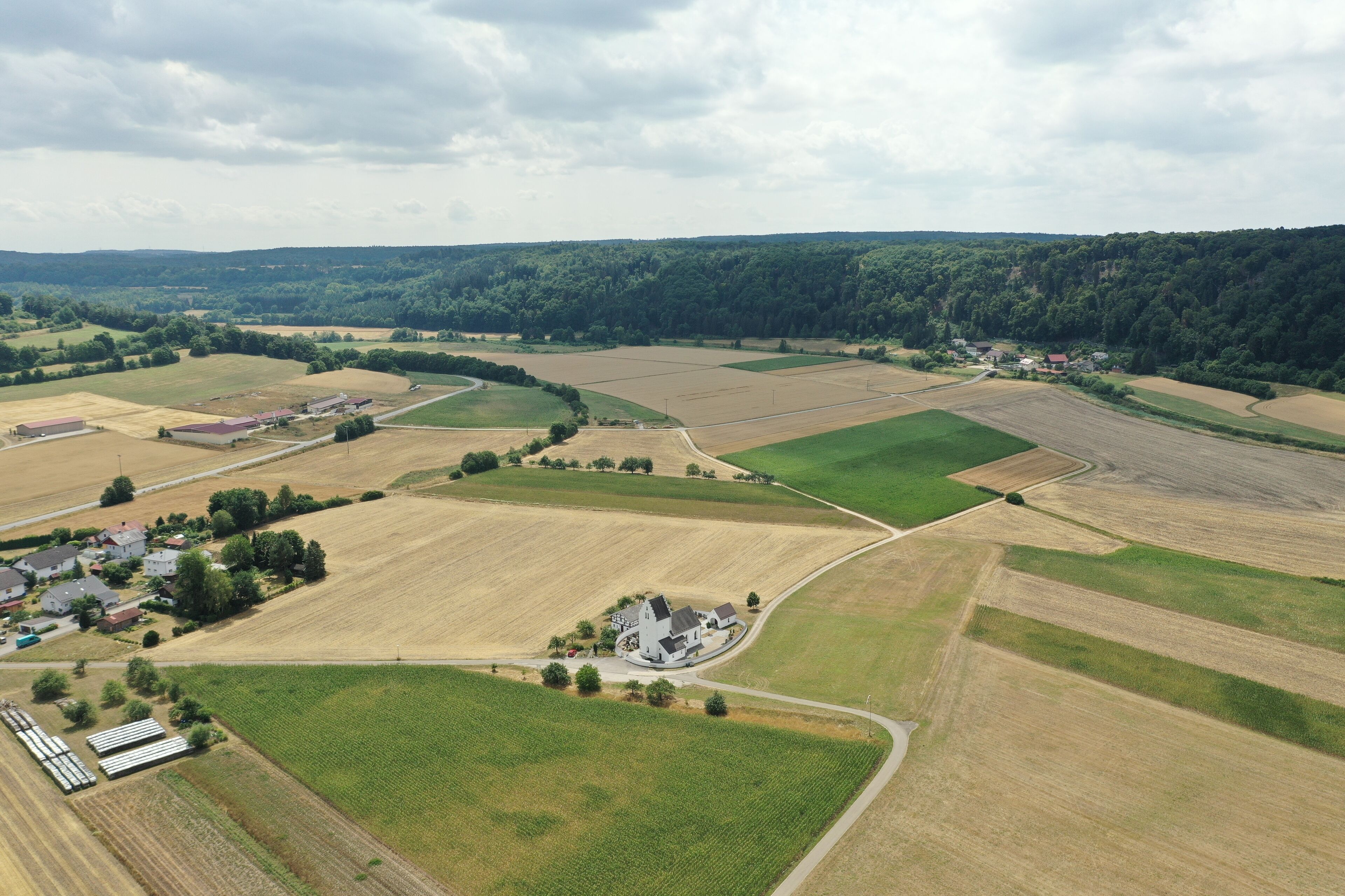 An aerial view of a rural landscape with fields, a small village, and a large white building surrounded by greenery.