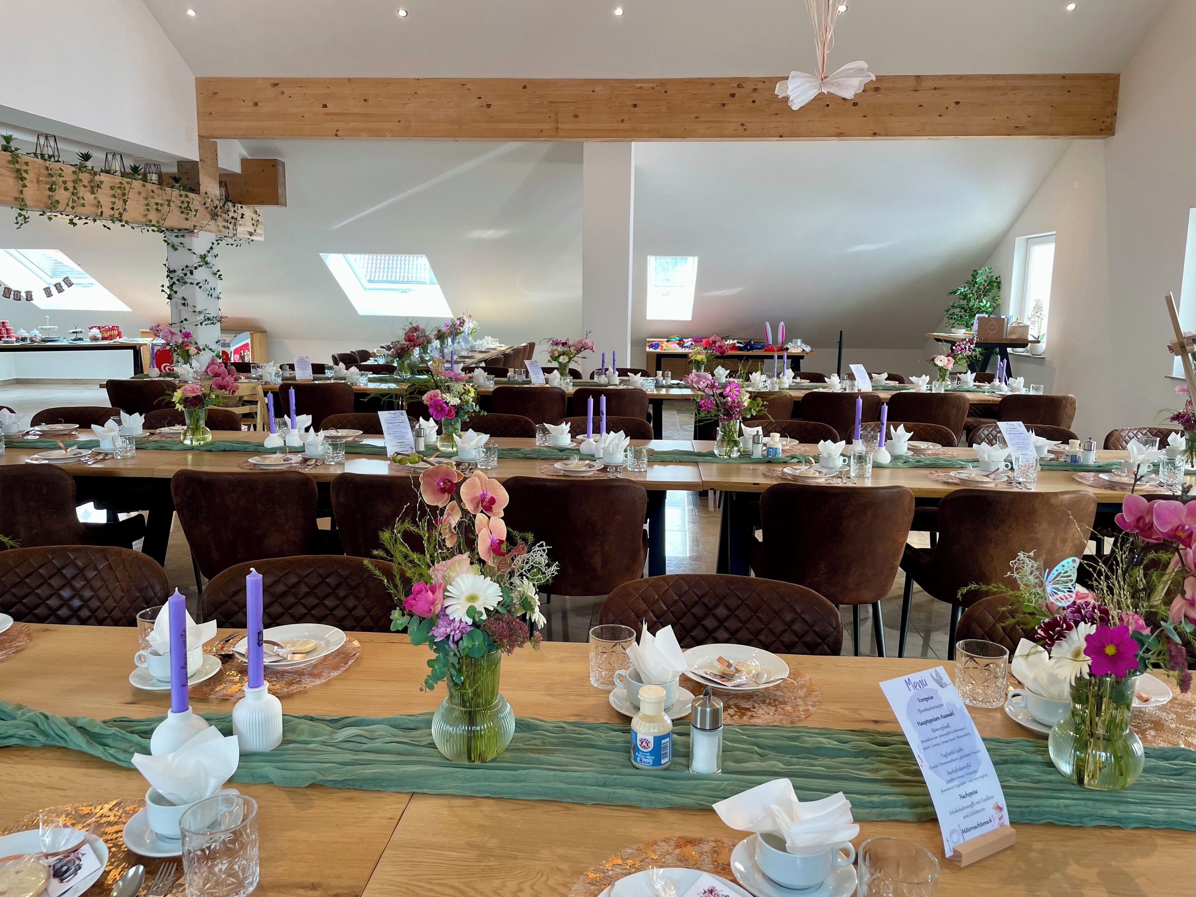 A spacious dining area with multiple tables set for service, featuring floral centerpieces and candles.