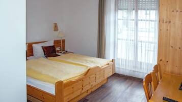A wooden bed with a yellow blanket, a wooden nightstand with a lamp, and a wooden table with a remote control.