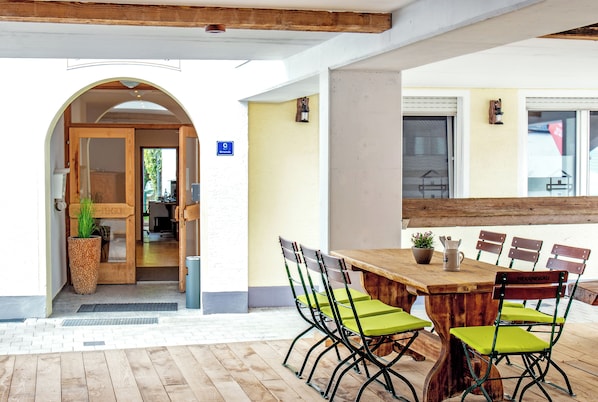 Una mesa de madera con sillas acolchadas verdes, una planta en maceta y un cartel con el número de una habitación.